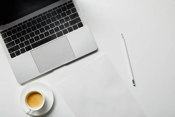 Draufsicht auf Laptop, Kaffee, Papier und Bleistift auf weißer Oberfläche — Stockfoto