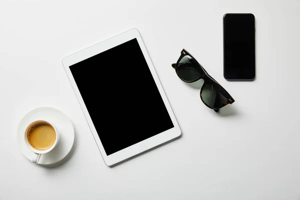 Vista superior de la tableta digital, café y vasos con teléfono inteligente en la superficie blanca - foto de stock