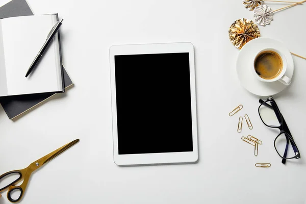 Vista superior de la tableta digital, papelería, tijeras, café, vasos y cuadernos con pluma en la superficie blanca - foto de stock