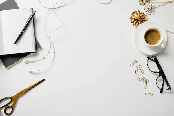 Vista superior de auriculares, artículos de papelería, tijeras, café, vasos y cuadernos con pluma en la superficie blanca - foto de stock