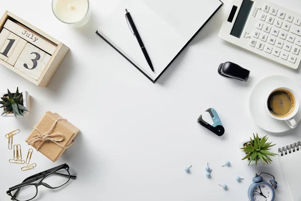 Top view of wooden calendar, notepad, pen, glasses, plants, coffee and office supplies on white surface — Stock Photo