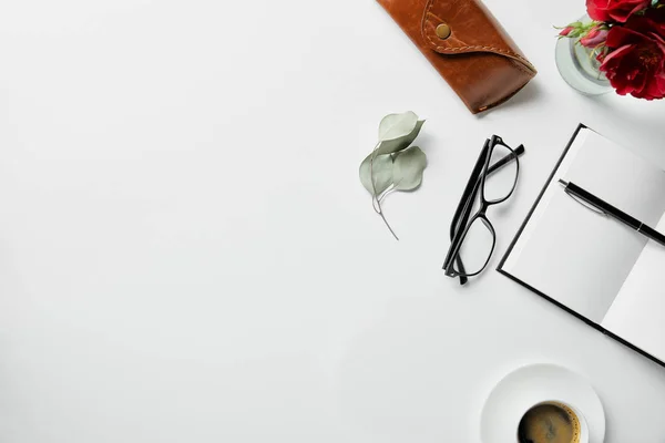 Vista superior del bloc de notas, bolígrafo, vasos, estuche, plantas y café en la superficie blanca - foto de stock