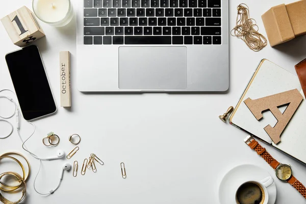 Vista superior do portátil, do smartphone, da jóia, da caixa, dos fones de ouvido, da vela, das flores, dos materiais de escritório e do café na superfície branca — Fotografia de Stock