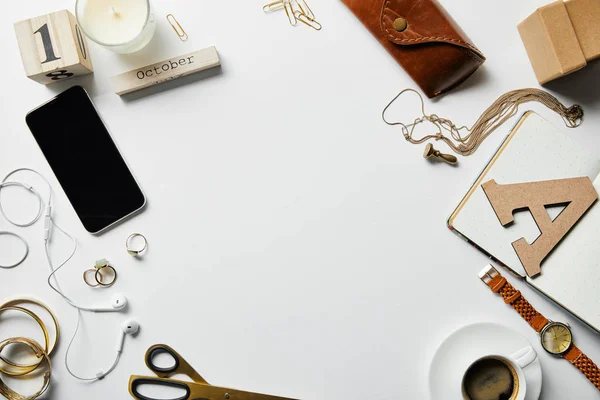 Vue du haut du smartphone, bloc-notes, bougie, étui, écouteurs, plantes, fournitures de bureau et café avec des bijoux sur la surface blanche — Photo de stock