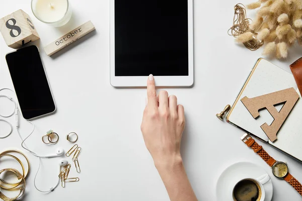 Cropped view of woman using digital tablet on white surface with plants, stationery, jewelry, notepad and coffee — Stock Photo