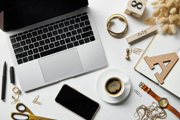 Vue de dessus de l'ordinateur portable et smartphone sur la surface blanche avec papeterie, plantes, bijoux, bloc-notes et café — Photo de stock