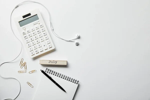 Vista superior de papelería, calculadora, auriculares y portátil con pluma en la superficie blanca - foto de stock