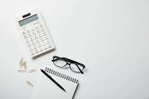 Vue du dessus de la papeterie, calculatrice et ordinateur portable avec stylo sur la surface blanche — Photo de stock