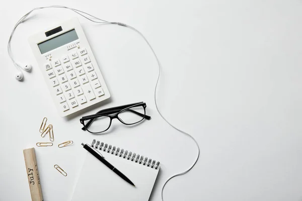 Vista dall'alto di cancelleria, calcolatrice, auricolari e notebook con penna su superficie bianca — Foto stock