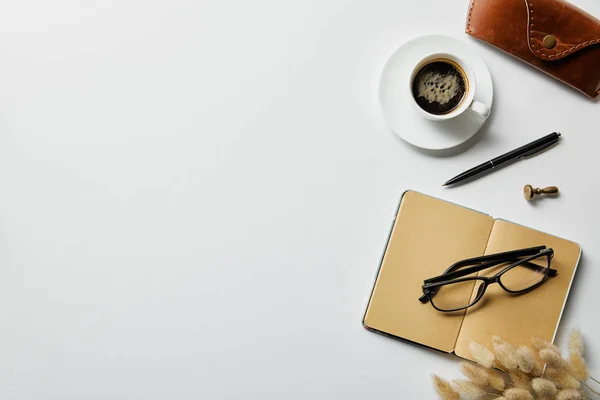 Vista superior de café, bloc de notas con pluma y estuche en la superficie blanca - foto de stock