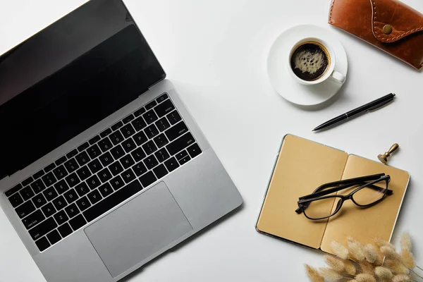 Vista superior do laptop perto de óculos, café, caixa e bloco de notas na superfície branca — Fotografia de Stock