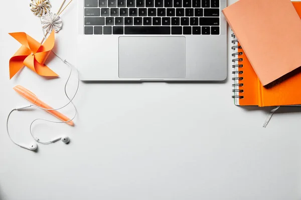Vista superior de bloc de notas naranja, auriculares, bolígrafo y portátil en la superficie blanca - foto de stock