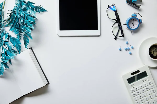 Top view of notepad, digital tablet, coffee, stationery, alarm clock, calculator, glasses and blue branch on white surface — Stock Photo