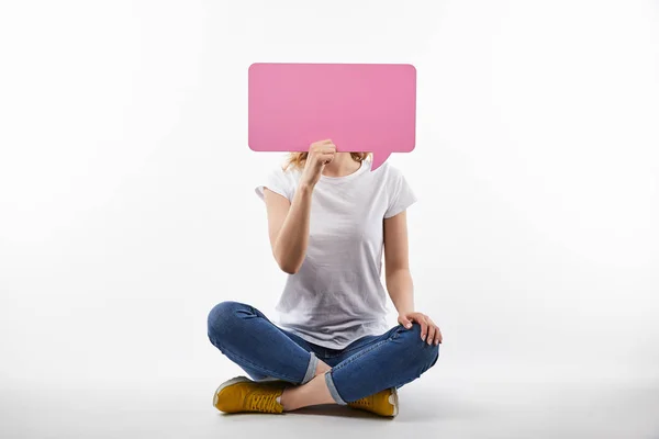 Mujer con burbuja de habla rosa en las manos sentado aislado en blanco - foto de stock