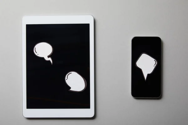 Smartphone with digital tablet and thought, speech bubbles on white surface — Stock Photo