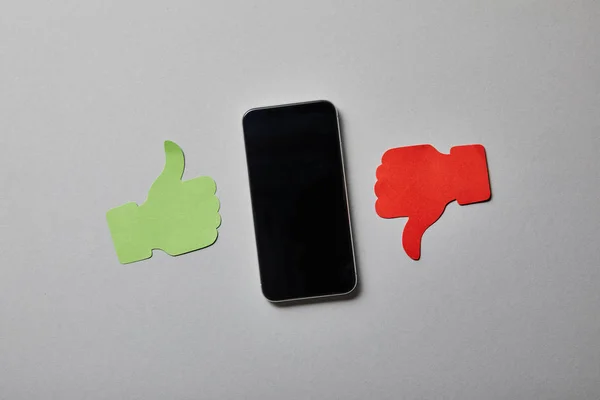 Smartphone in der Nähe Daumen hoch und Daumen runter Papierschild auf weißer Oberfläche — Stockfoto