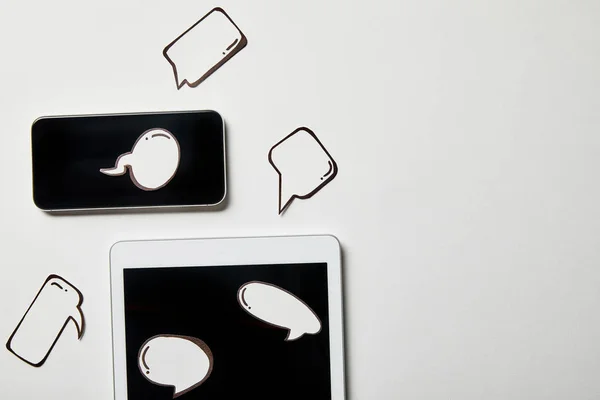 Tableta digital y teléfono inteligente con burbujas de pensamiento y voz de papel en la superficie blanca - foto de stock