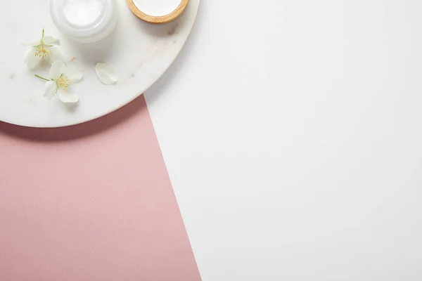 Vue de dessus de la plaque avec crème et fleurs sur la surface rose blanc — Photo de stock