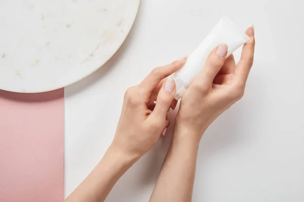 Cropped view of woman holding cream tube in hands near plate on white pink surface — Stock Photo