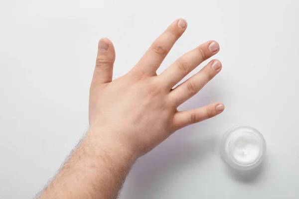 Vista ritagliata dell'uomo che tiene la mano sulla superficie bianca con crema cosmetica in vaso — Foto stock