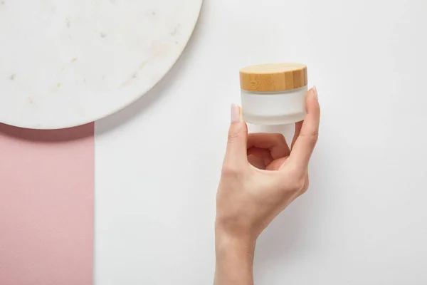 Cropped view of woman holding cream in jar near plate on white pink surface — Stock Photo
