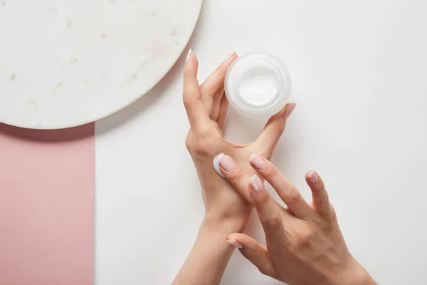 Vista cortada de mulher segurando creme no frasco, aplicando cosmético na pele — Fotografia de Stock