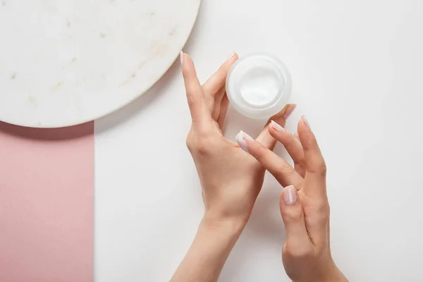 Vista ritagliata di donna che tiene la crema in vaso, applicando il cosmetico su pelle — Foto stock
