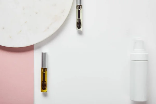 Draufsicht auf Wimperntuschflaschen und Kosmetikspender in Tellernähe auf weiß-rosa Oberfläche — Stockfoto
