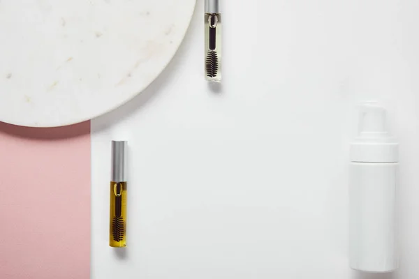 Top view of mascara bottles and cosmetic dispenser near plate on white pink surface — Stock Photo