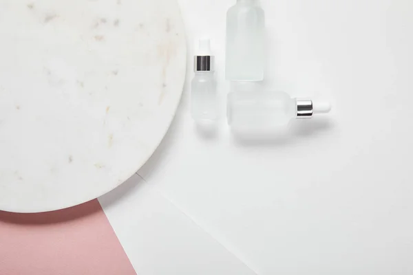 Вид зверху косметичних скляних пляшок біля пластини на біло-рожевій поверхні — стокове фото