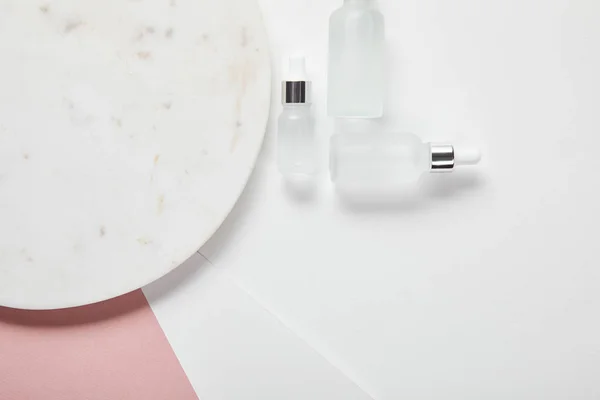 Top view of cosmetic glass bottles near plate on white pink surface — Stock Photo