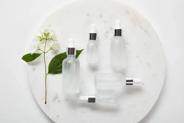 Vue de dessus de la plaque avec du jasmin et des bouteilles en verre cosmétique sur la surface blanche — Photo de stock