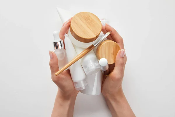 Vista cortada de mãos de mulher com cosméticos em tubos, dispensadores, garrafas e frasco isolado em branco — Fotografia de Stock