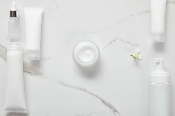 Vue du dessus de la bouteille en verre cosmétique, pot avec crème, tubes hydratants, distributeur et jasmin sur surface blanche — Photo de stock