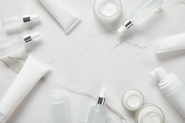 Vue du dessus des bouteilles en verre cosmétique, bocal avec crème, tubes hydratants, distributeur et jasmin sur surface blanche — Photo de stock