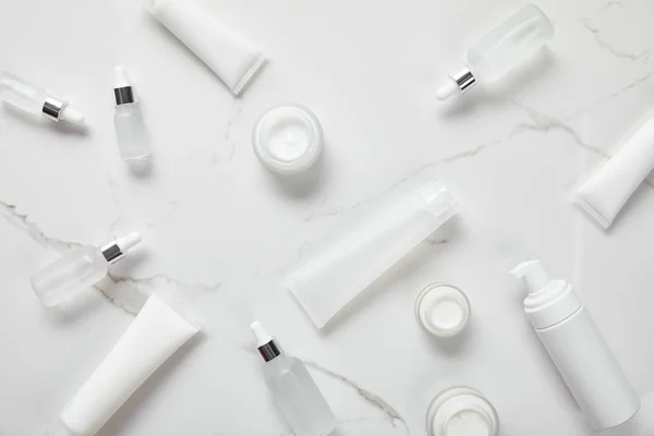 Vue du dessus des bouteilles en verre cosmétique, bocaux avec crème, tubes hydratants, distributeur et jasmin sur surface blanche — Photo de stock