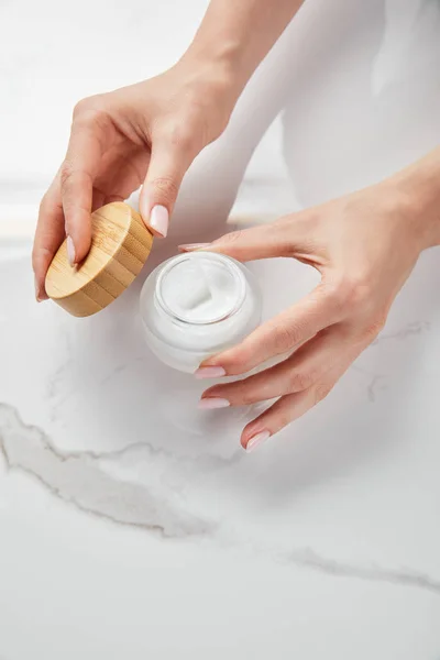 Vista ritagliata della donna vaso di apertura con crema sulla superficie bianca — Foto stock