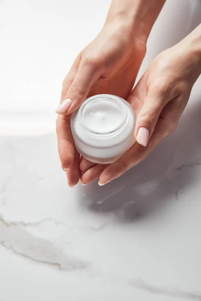 Cropped view of woman holding jar with cream on white surface — Stock Photo