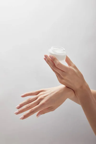 Vista cortada de mãos de mulher segurando frasco com creme isolado no branco — Fotografia de Stock