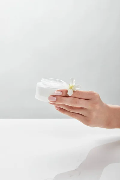 Cropped view of woman holding jar with cream and jasmine in hand — Stock Photo