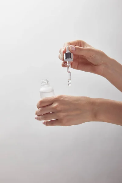 Vista recortada de la mujer sosteniendo botella de vidrio cosmético, aplicando suero hidratante en la piel - foto de stock