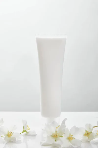 Flores de jazmín en la superficie blanca cerca de la crema cosmética en tubo - foto de stock