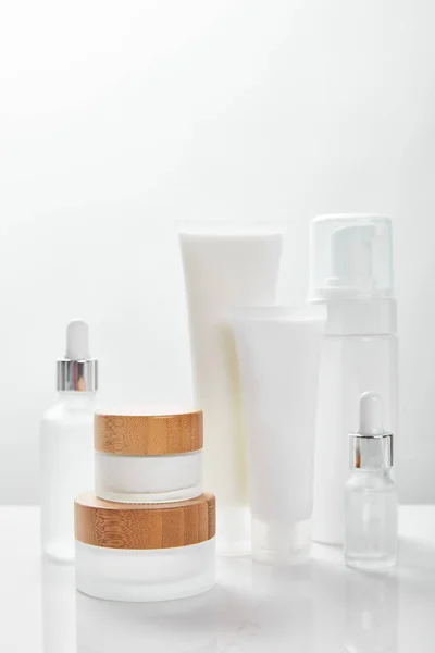Superfície branca com garrafas de vidro, creme em tubos, frascos e dispensador de cosméticos — Fotografia de Stock
