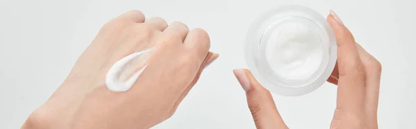 Colpo panoramico di donna che applica la crema su pelle e tiene il vaso isolato su bianco — Foto stock