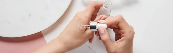 Panoramic shot of woman applying liquid from glass bottle on white surface — Stock Photo