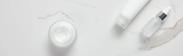 Colpo panoramico di bottiglia di vetro cosmetico, vaso con crema e tubo idratante su superficie bianca — Foto stock