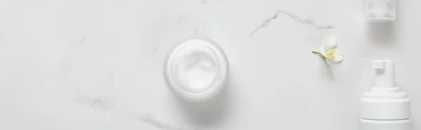Plano panorámico de jazmín, frasco con dispensadores de crema y cosméticos en la superficie blanca - foto de stock