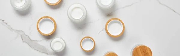 Plano panorámico de frascos con crema cosmética y tapas de madera en la superficie blanca - foto de stock