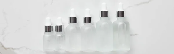 Panoramic shot of cosmetic glass bottles on white surface — Stock Photo
