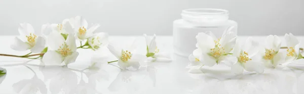 Plano panorámico de flores de jazmín en la superficie blanca cerca del frasco con crema - foto de stock